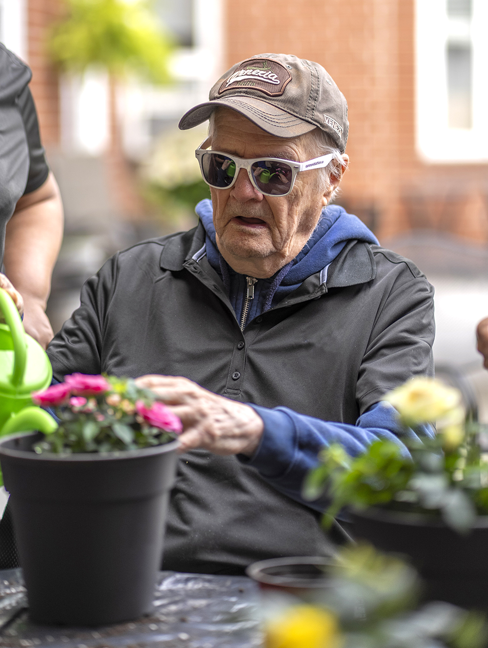 Male resident wearing sunglasses while gardening outdoors with potted plants.