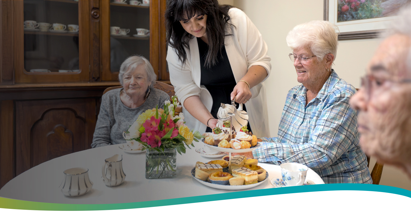 Server pouring afternoon tea for a group of smiling residents enjoying treats together at Atrium Retirement Residence in Orillia.