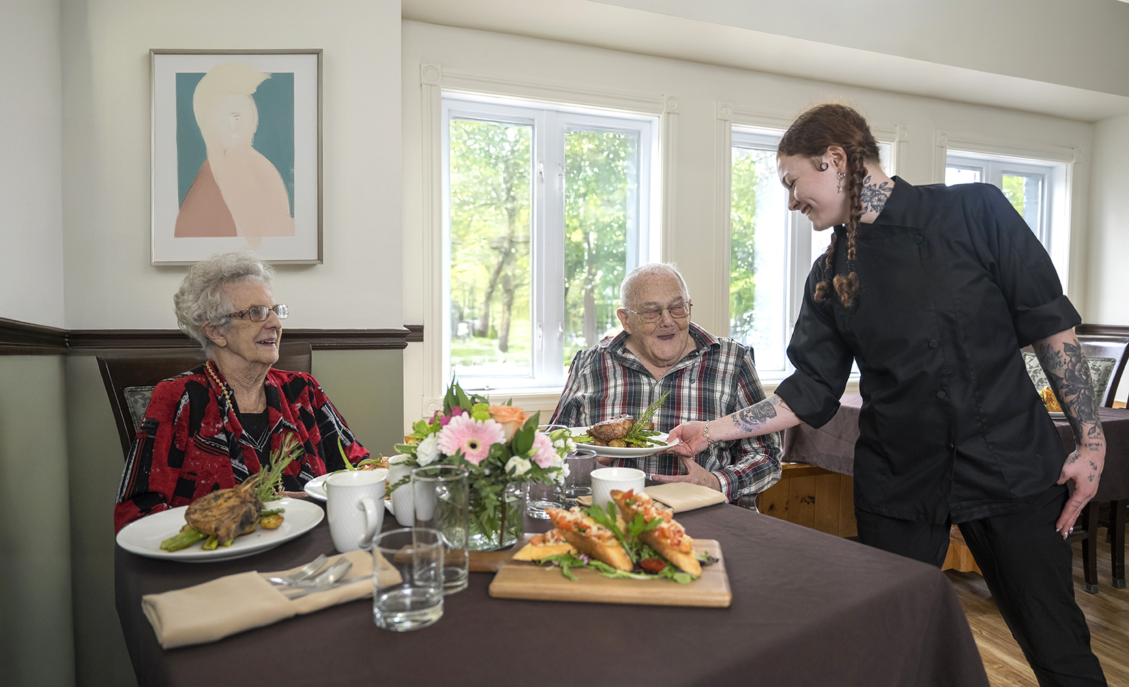 Couple being served dinner as server smiles a them at ATrium retirement residence