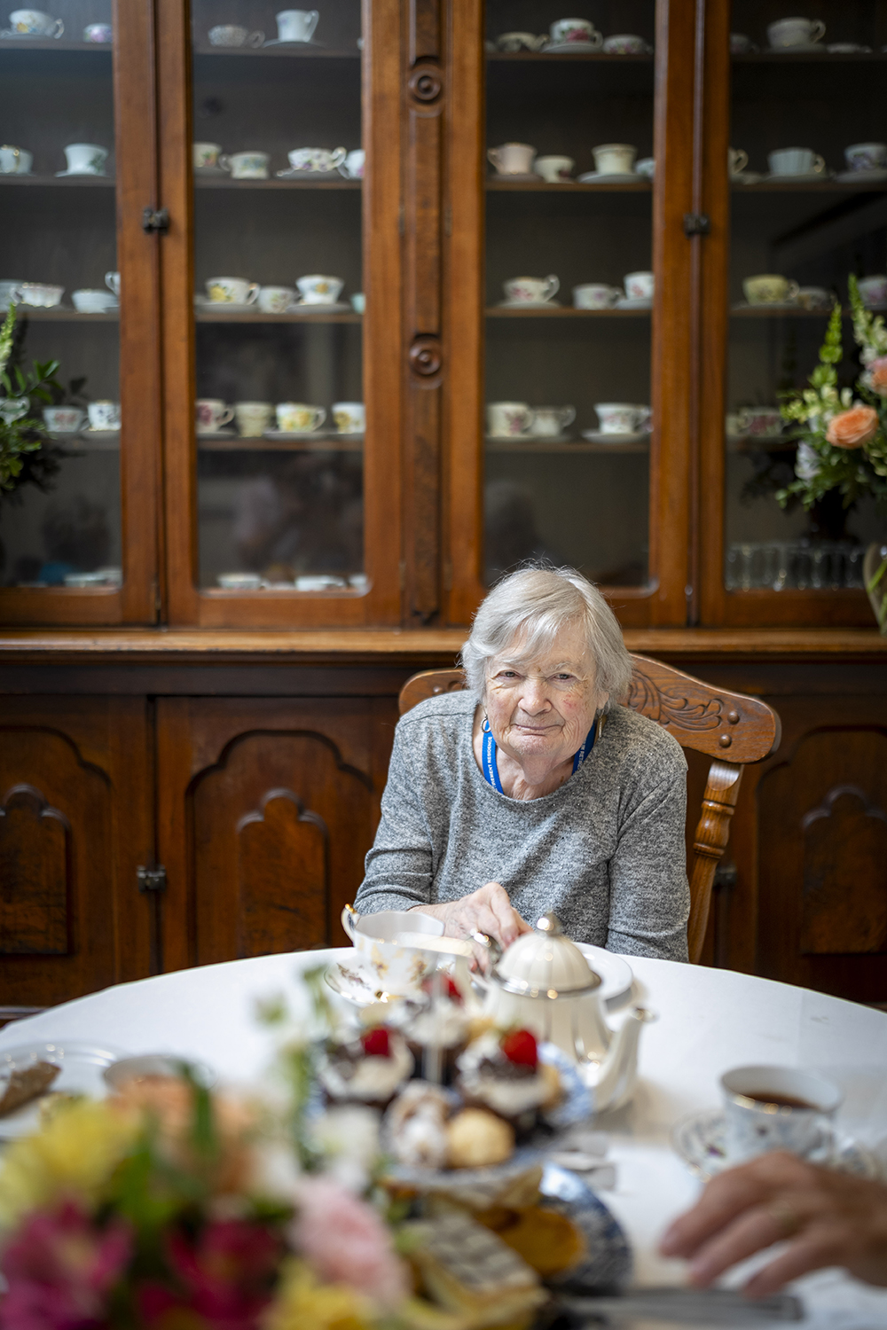Resident enjoying afternoon tea with a tray of treats beside a traditional wooden china cabinet.